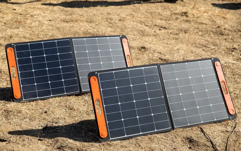 Twee opvouwbare zonnepanelen met oranje randen op een zanderige ondergrond
